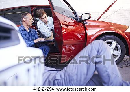 Mechanics with laptop talking at car in auto repair shop View Large Photo Image Picture - Mechanics with laptop talking at car in auto repair shop. Fotosearch