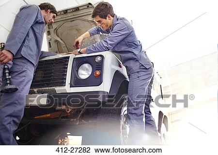 Stock Image - Mechanics working on engine in auto repair shop. Fotosearch