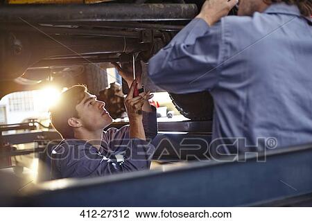 Stock Image - Mechanics working under car in auto repair shop. Fotosearch