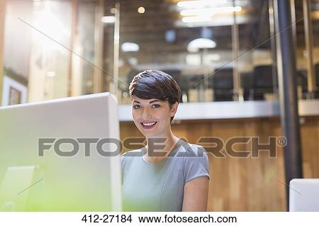 Picture - Portrait smiling businesswoman working at computer in office. Fotosearch