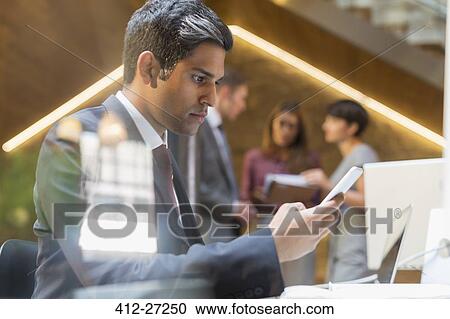 Stock Image - Serious businessman texting with cell phone in office. Fotosearch