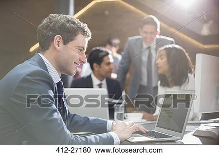 Smiling businessman working at laptop in office View Large Photo Image Stock Image - Smiling businessman working at laptop in office. Fotosearch