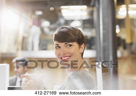 Stock Photo - Smiling businesswoman drinking coffee in office. Fotosearch