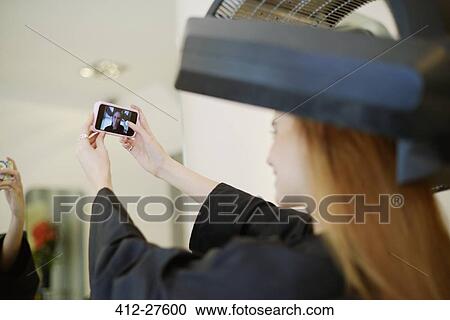 Stock Image - Customer taking selfie with camera phone in hair salon. Fotosearch
