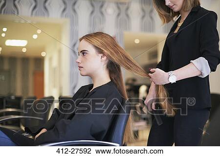 Stock Image - Hairdresser preparing to cut customer’s long hair in salon. Fotosearch