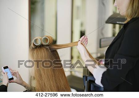 Stock Photograph - Hairdresser rolling customer’s hair in curlers in salon. Fotosearch