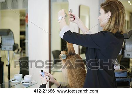 Stock Photograph - Hairdresser wrapping customer’s hair in curlers in salon. Fotosearch