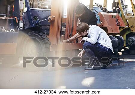 Mechanic and customer examining forklift in auto repair shop View Large Photo Image Picture - Mechanic and customer examining forklift in auto repair shop. Fotosearch