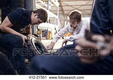 Stock Image - Mechanic and customer examining tire in auto repair shop. Fotosearch