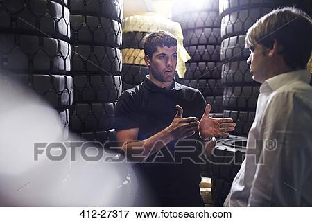 Stock Photo - Mechanic and customer talking near stacked tires. Fotosearch