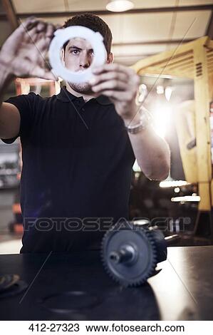 Stock Image - Mechanic examining part in auto repair shop. Fotosearch