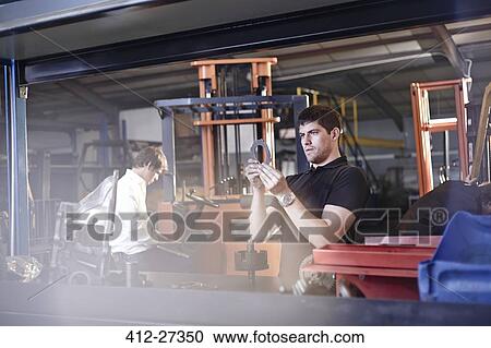 Stock Image - Mechanic examining part in auto repair shop. Fotosearch