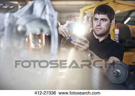 Stock Photograph - Mechanic examining part in auto repair shop. Fotosearch