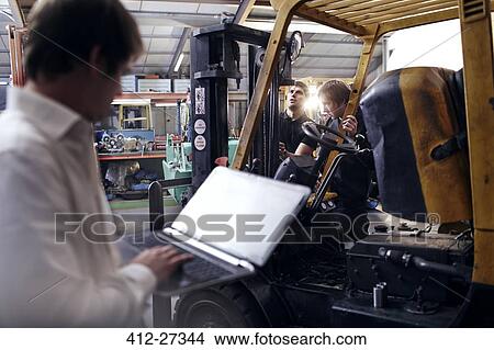 Picture - Mechanic using laptop next to forklift in auto repair shop. Fotosearch