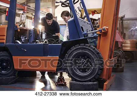 Stock Photo - Mechanics examining forklift in auto repair shop. Fotosearch