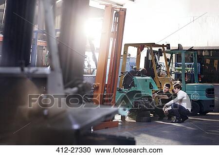 Stock Image - Mechanics fixing forklift in auto repair shop. Fotosearch