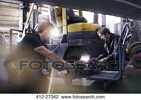 Stock Image - Mechanics fixing forklift in auto repair shop. Fotosearch