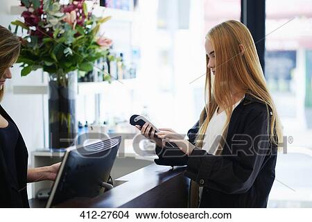 Woman paying with credit card reader at counter in hair salon View Large Photo Image Picture - Woman paying with credit card reader at counter in hair salon. Fotosearch