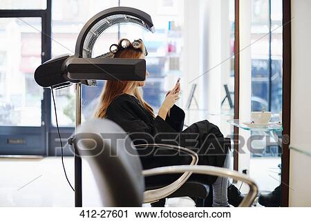 Woman sitting under dryer texting with cell phone in hair salon View Large Photo Image Stock Image - Woman sitting under dryer texting with cell phone in hair salon. Fotosearch