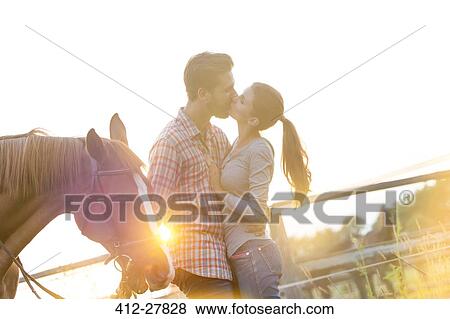 Affectionate couple kissing next to horse in sunny rural pasture View Large Photo Image Stock Photo - Affectionate couple kissing next to horse in sunny rural pasture. Fotosearch