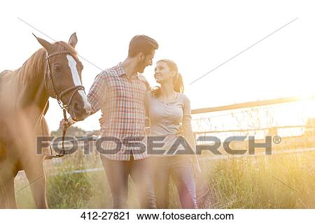 Affectionate couple walking with horse in rural pasture View Large Photo Image Stock Image - Affectionate couple walking with horse in rural pasture. Fotosearch