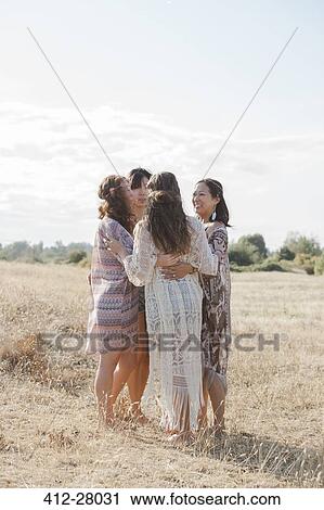 Stock Image - Boho women hugging in a circle in sunny rural field. Fotosearch