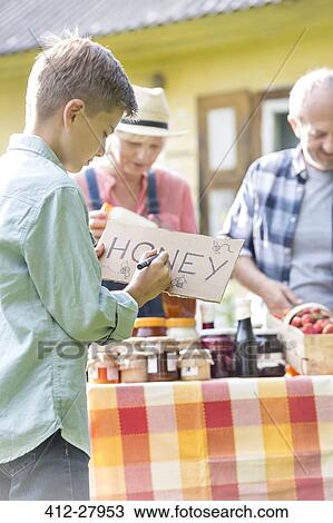 Stock Image - Boy drawing honey sign for farmer’s market stall. Fotosearch