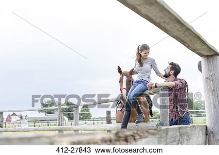 Stock Image - Couple and horse at rural pasture fence. Fotosearch