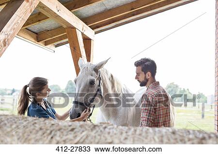 Stock Image - Couple petting horse in rural stable. Fotosearch