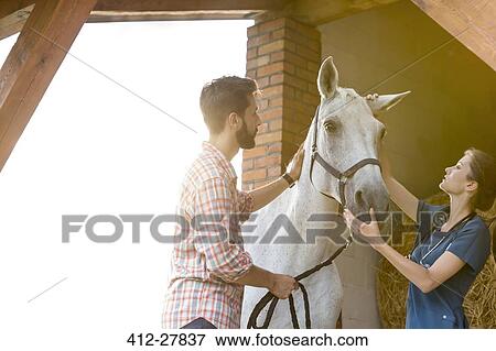 Stock Photo - Couple petting horse in rural stable. Fotosearch