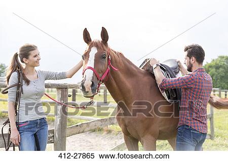 Couple saddling horse in rural pasture View Large Photo Image Stock Photography - Couple saddling horse in rural pasture. Fotosearch