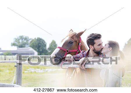 Stock Photo - Couple with horse kissing at rural pasture fence. Fotosearch
