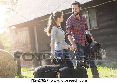 Couple with saddle and dogs holding hands outside rural barn View Large Photo Image Stock Photo - Couple with saddle and dogs holding hands outside rural barn. Fotosearch