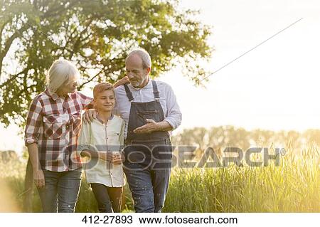 Stock Image - Grandparent farmers and grandson walking along rural wheat field. Fotosearch