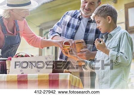 Grandparents and grandson tasting and selling honey at farmer’s market stall View Large Photo Image Stock Image - Grandparents and grandson tasting and selling honey at farmer’s market stall. Fotosearch