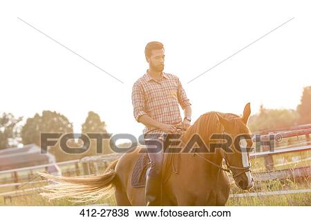 Man horseback riding in sunny rural pasture View Large Photo Image Stock Photo - Man horseback riding in sunny rural pasture. Fotosearch