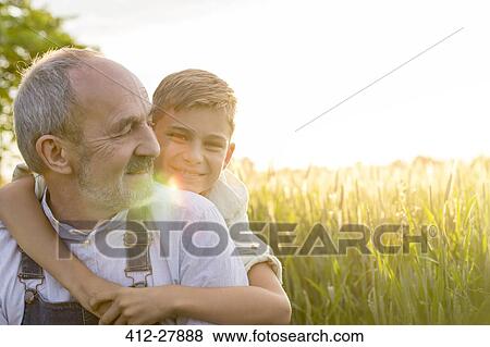Stock Photo - Portrait affectionate grandson hugging grandfather in rural wheat field. Fotosearch