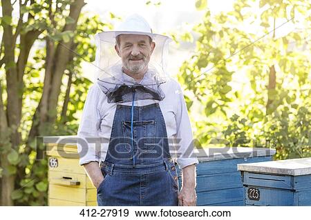 Portrait confident beekeeper in protective hat next to beehives View Large Photo Image Stock Photo - Portrait confident beekeeper in protective hat next to beehives. Fotosearch