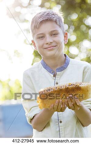 Stock Photography - Portrait confident boy holding fresh honeycomb. Fotosearch