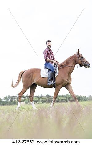 Stock Image - Portrait smiling man horseback riding in rural field. Fotosearch