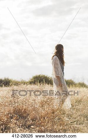 Stock Photograph - Serene boho woman standing in rural field. Fotosearch