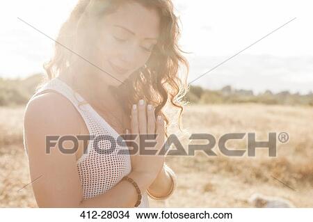 Picture - Serene boho woman with hands at heart center in sunny rural field. Fotosearch