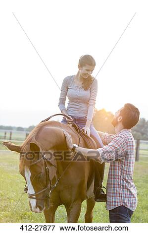Stock Photo - Smiling couple horseback riding in rural pasture. Fotosearch