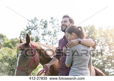 Stock Photography - Smiling couple hugging near horse. Fotosearch