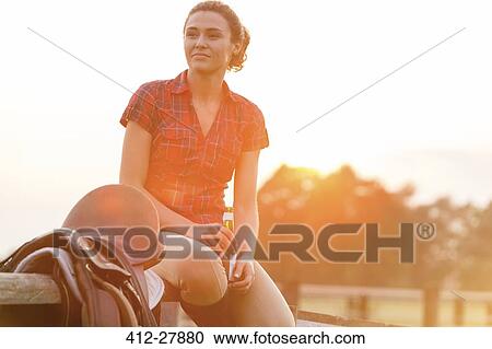 Smiling woman drinking beer next to saddle on rural fence View Large Photo Image Stock Image - Smiling woman drinking beer next to saddle on rural fence. Fotosearch