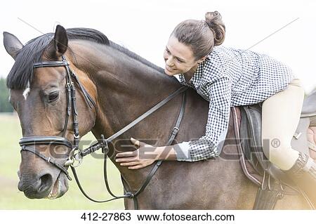 Smiling woman horseback riding leaning and petting horse View Large Photo Image Stock Image - Smiling woman horseback riding leaning and petting horse. Fotosearch