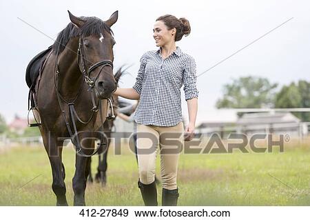 Smiling woman walking horse in rural pasture View Large Photo Image Stock Photo - Smiling woman walking horse in rural pasture. Fotosearch