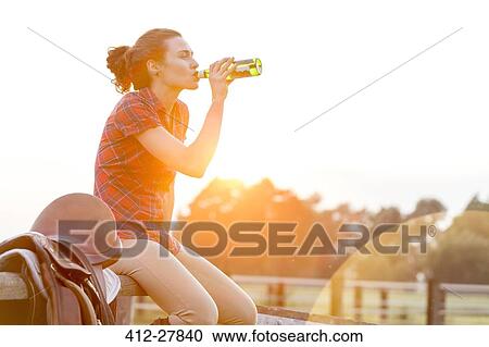 Woman drinking water next to saddle on rural fence View Large Photo Image Stock Image - Woman drinking water next to saddle on rural fence. Fotosearch