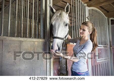 Stock Photo - Woman feeding horse at stable stall. Fotosearch