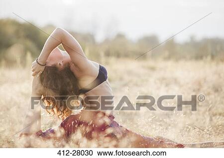 Stock Image - Woman in royal king pigeon yoga pose in rural field. Fotosearch